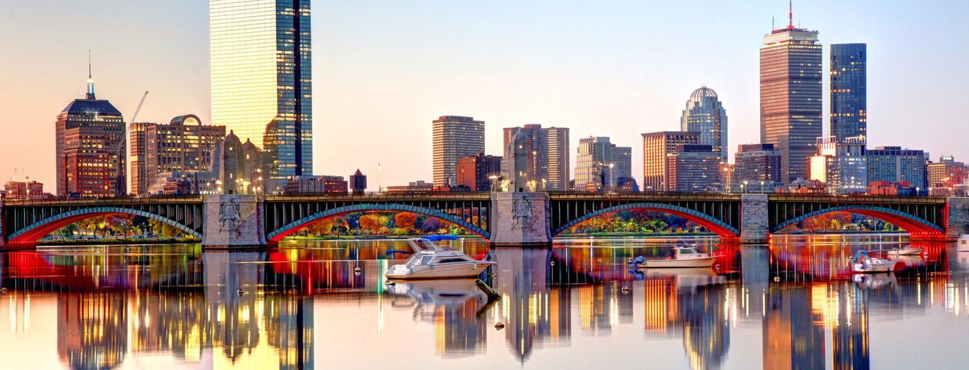Boston skyline reflected in the Charles River behind an arched bridge
