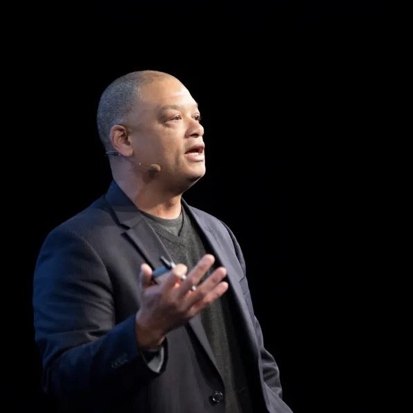 Charley Moore speaking onstage, wearing a headset microphone