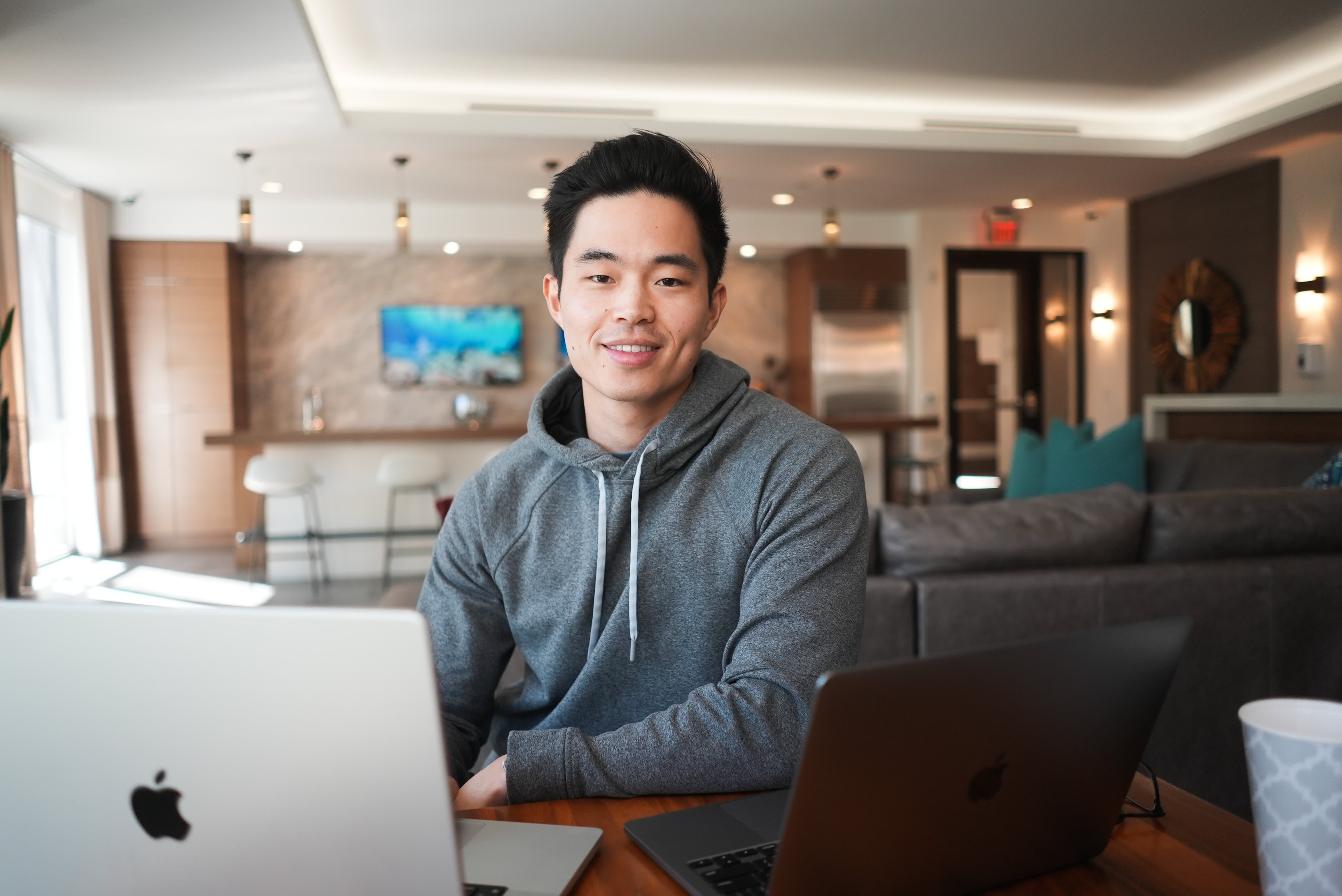 Charlie Chang sitting with two laptops at a wooden table