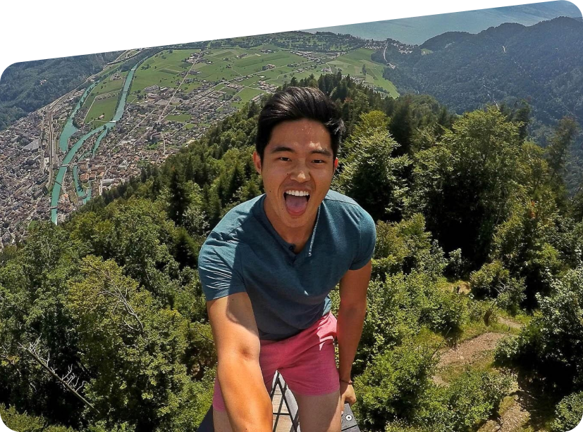 Charlie Chang smiling toward a camera outdoors above a tree lined valley