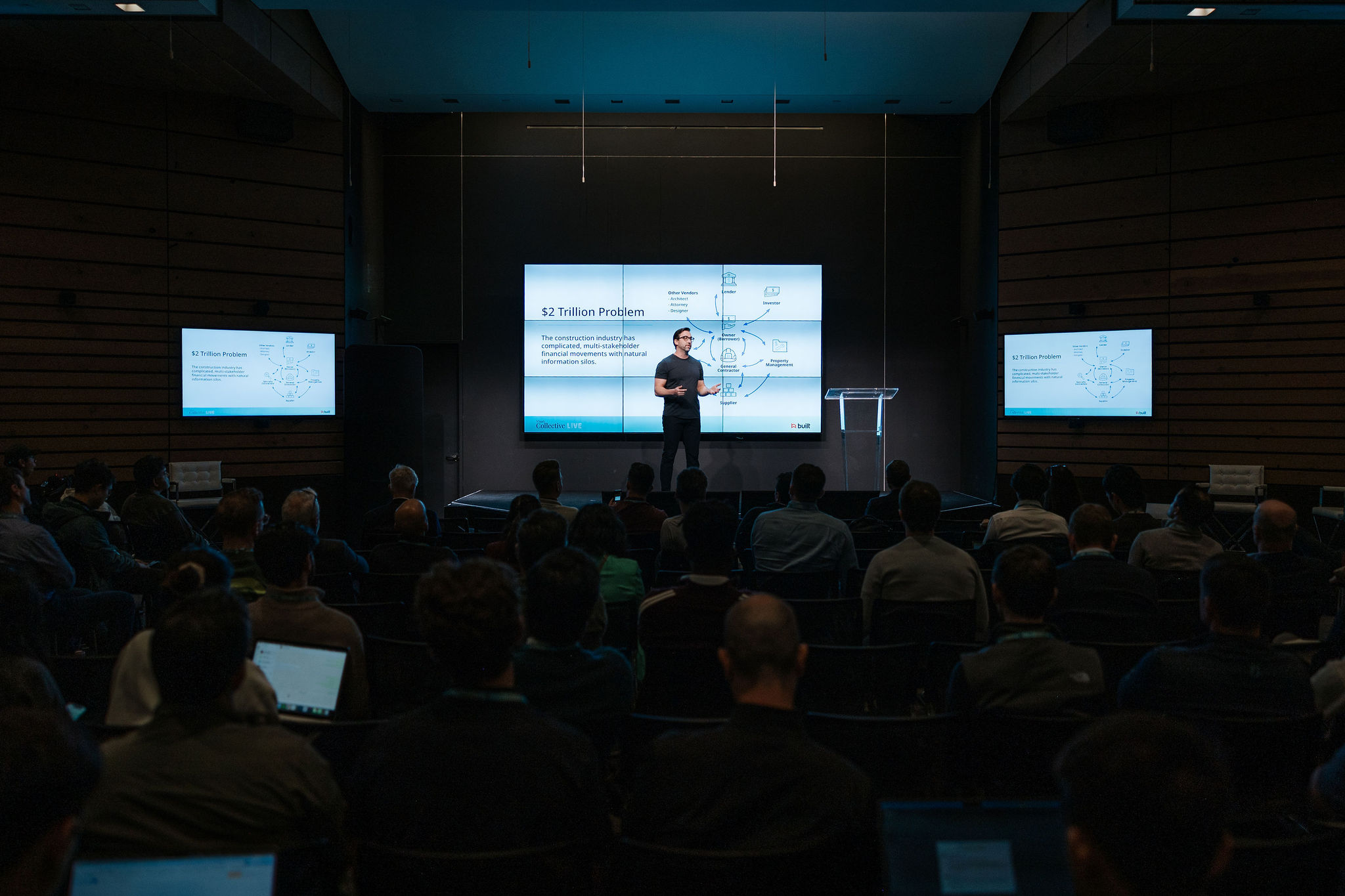 Chase Gilbert speaking onstage at a VSaaS Collective Live event, with a construction finance diagram behind him