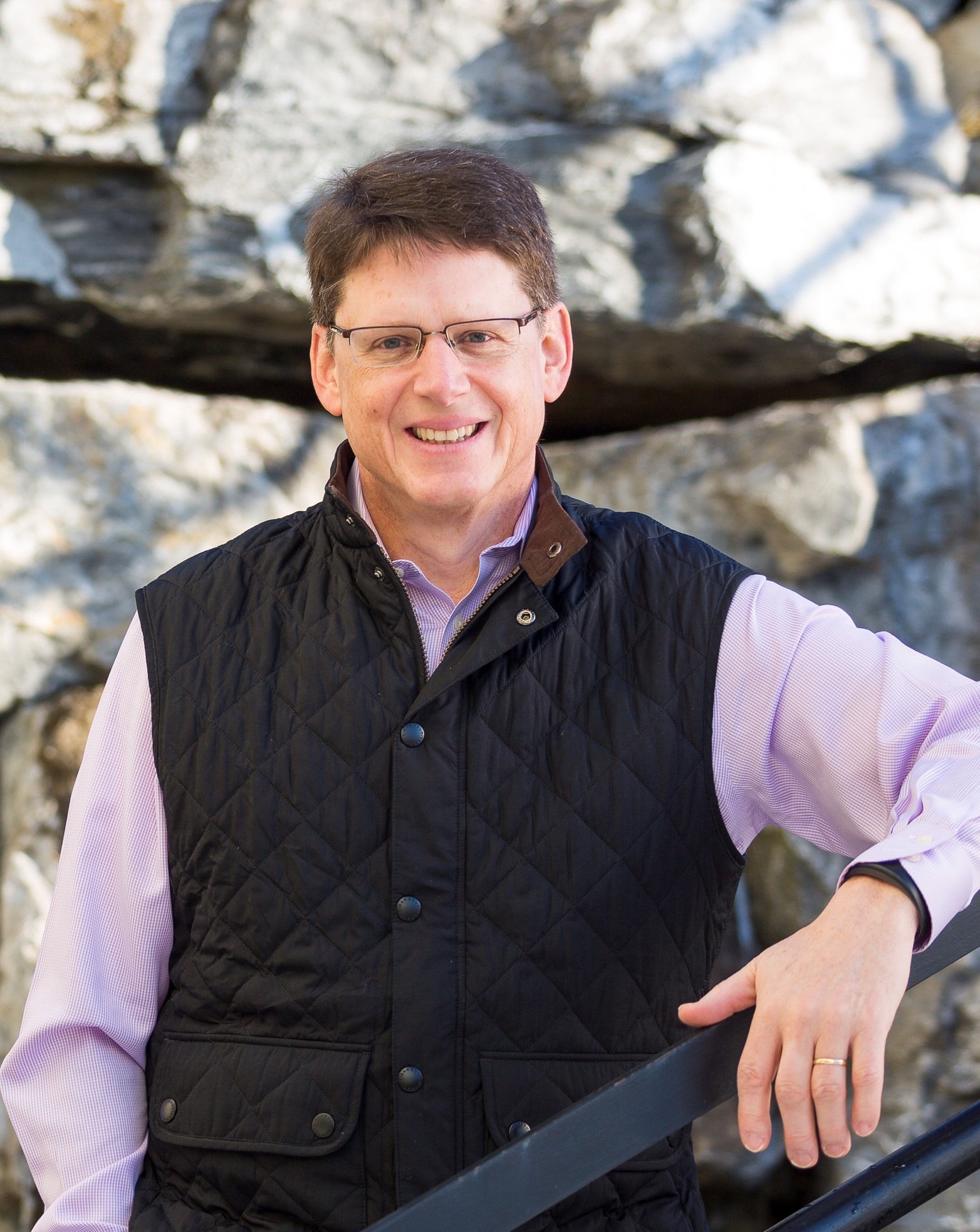 Chatham Financial founder Michael Bontrager wearing glasses and a quilted vest beside a stone wall