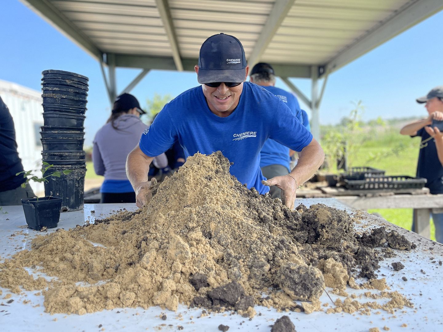 A Cheniere volunteer working with soil and planting pots during a community activity