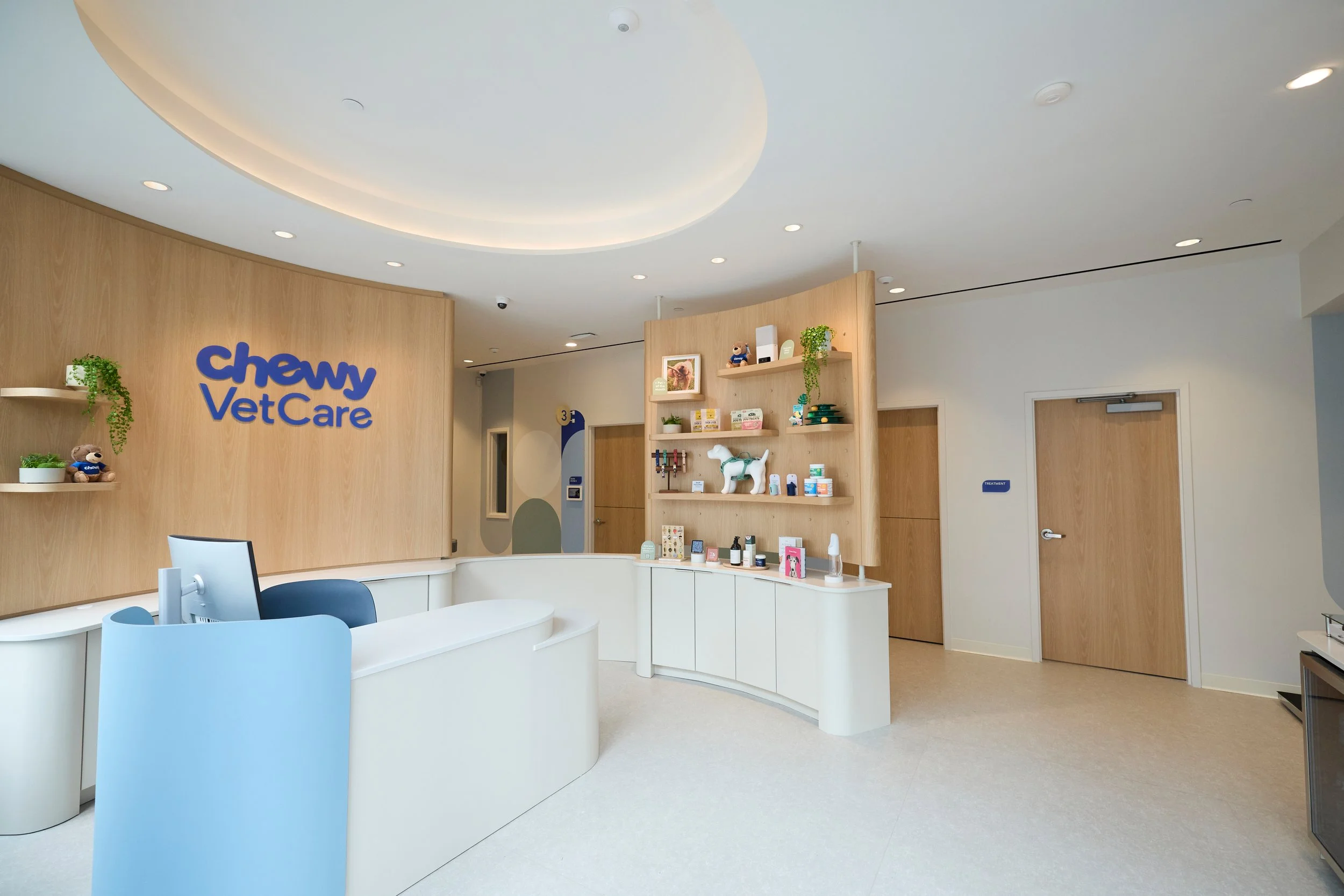 Curved reception desk, wood shelving and exam-room doors at a Chewy Vet Care clinic