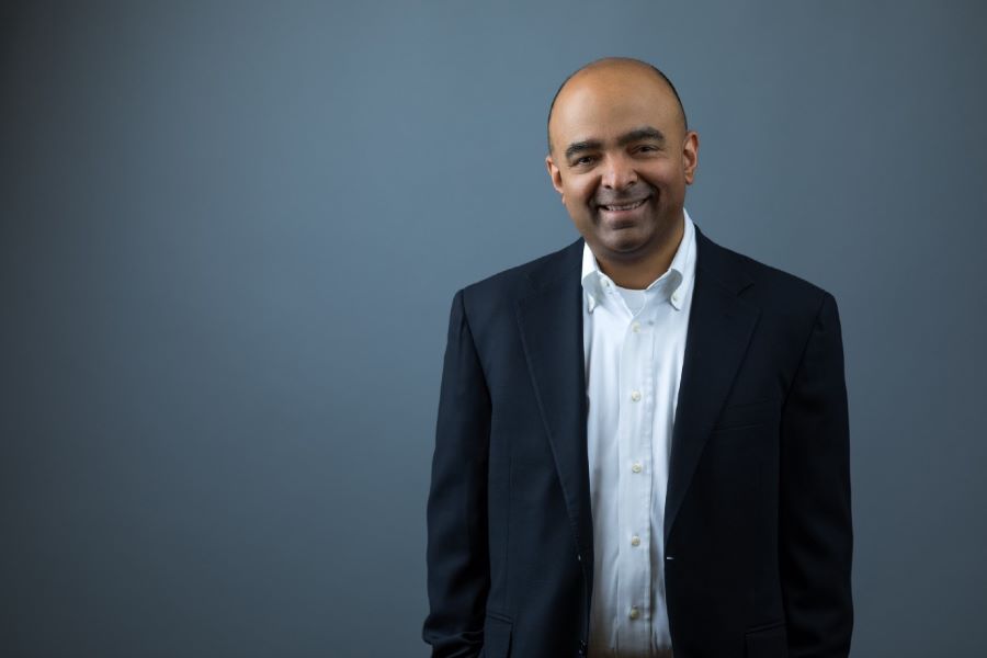 Chini Krishnan standing in a dark jacket against a blue-gray background