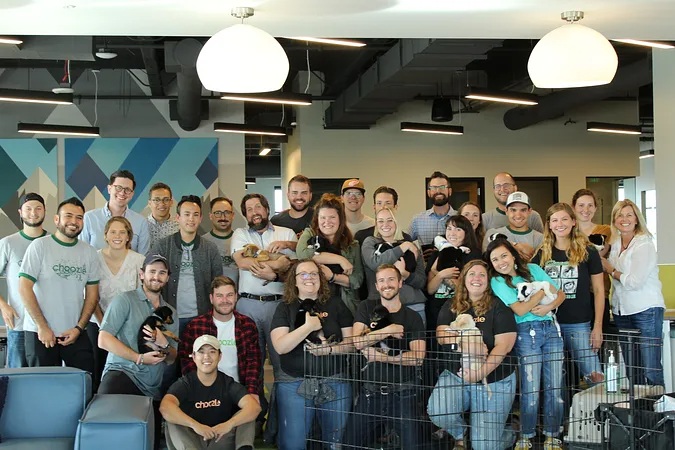 An archival Choozle office gathering, with employees holding puppies beside a playpen.