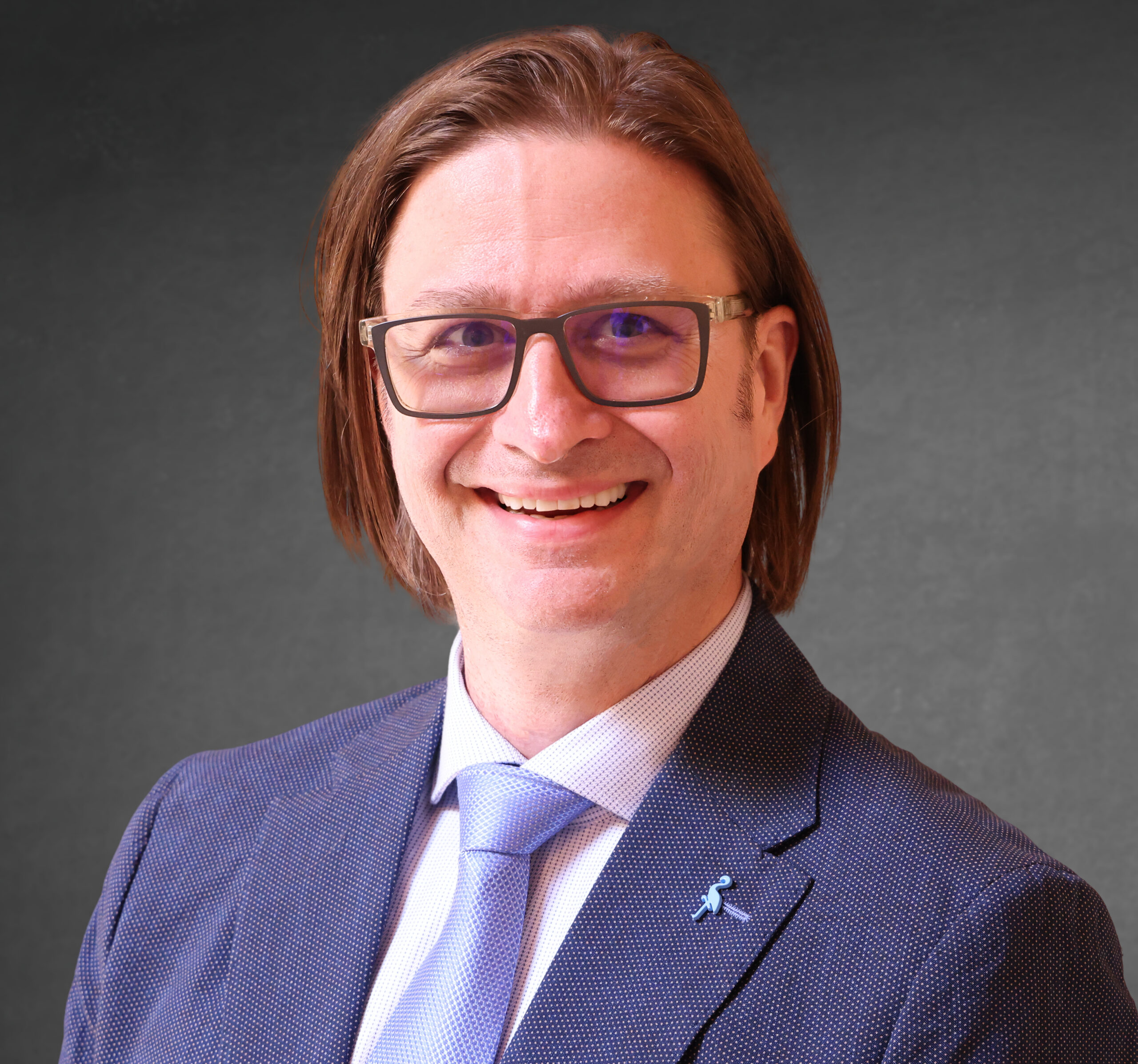 Chris Burns in a navy suit and glasses against a dark studio background