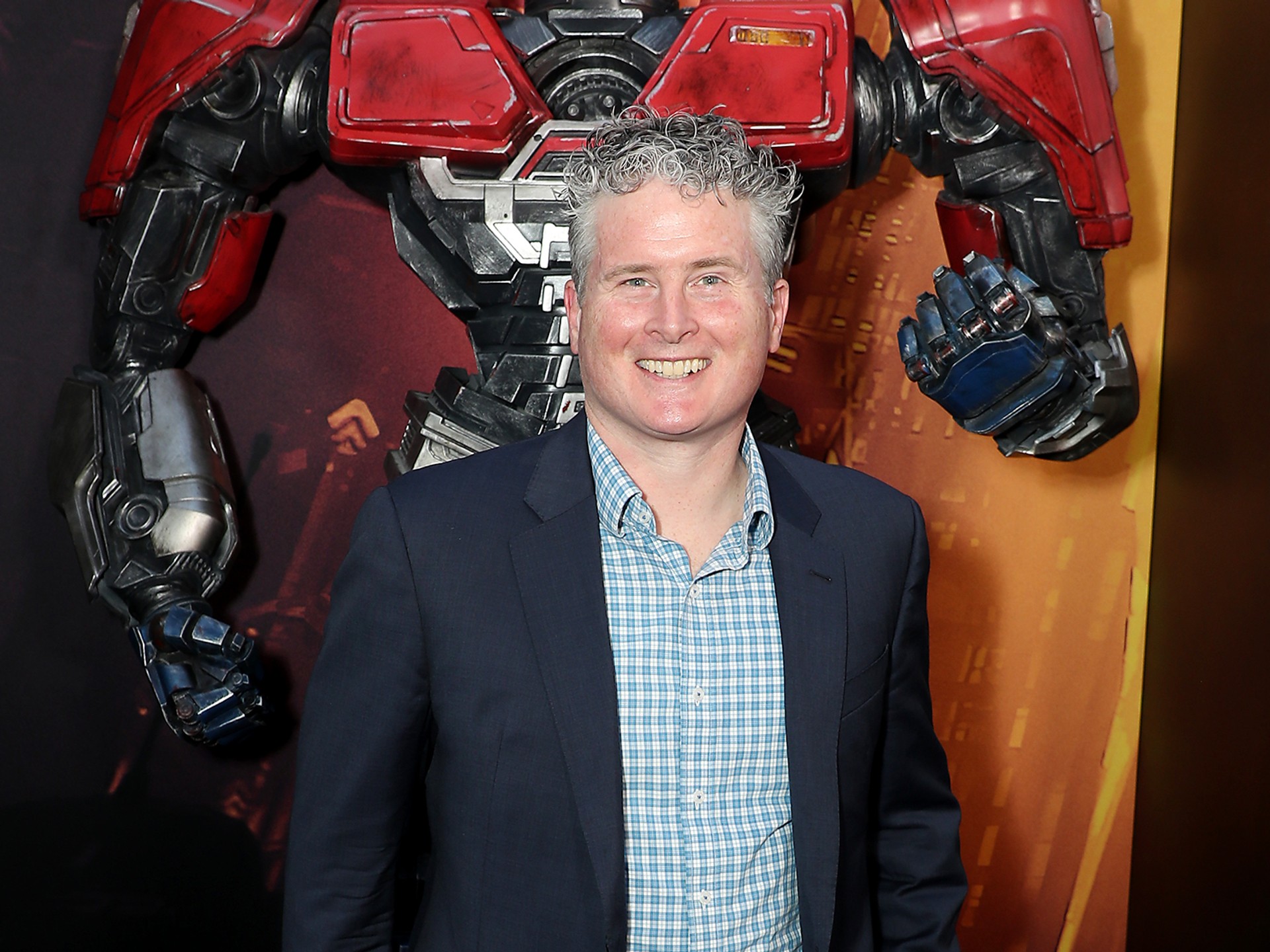 Chris Cocks in a navy jacket, standing in front of a large red robot display