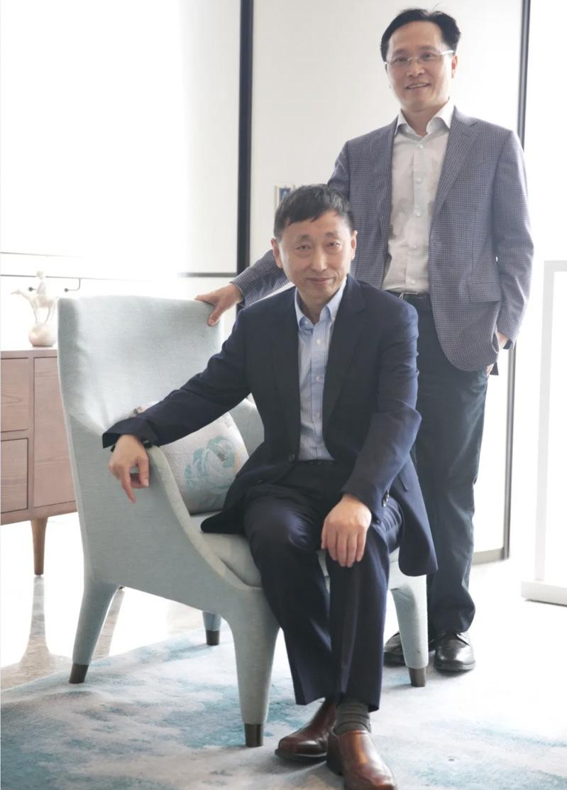 William Jia seated beside Chris Huang, who is standing, in an office