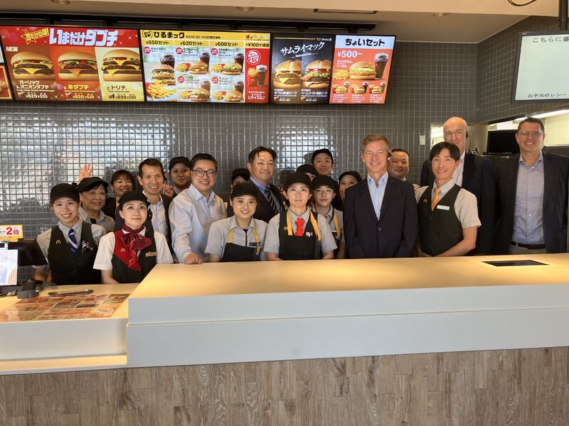 Chris Kempczinski joins McDonald’s Japan colleagues for a group photograph behind a restaurant counter.