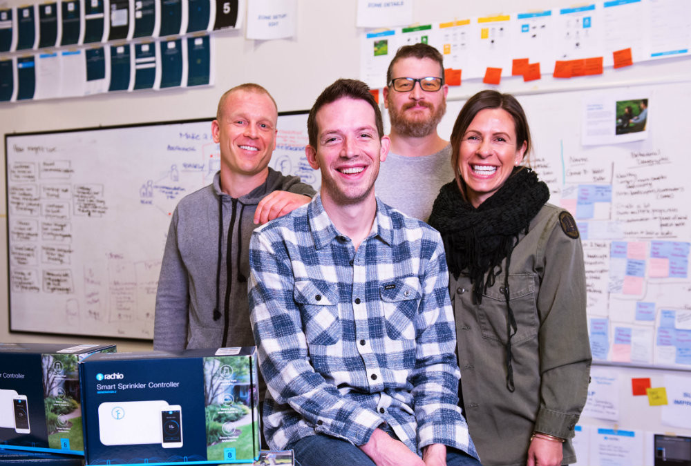 Chris Klein, front center in a checked shirt, with three Rachio colleagues in their workspace