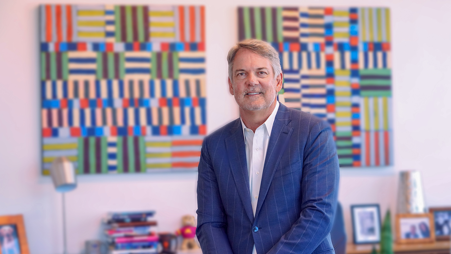 Chris Koch seated in an office with colorful artwork behind him