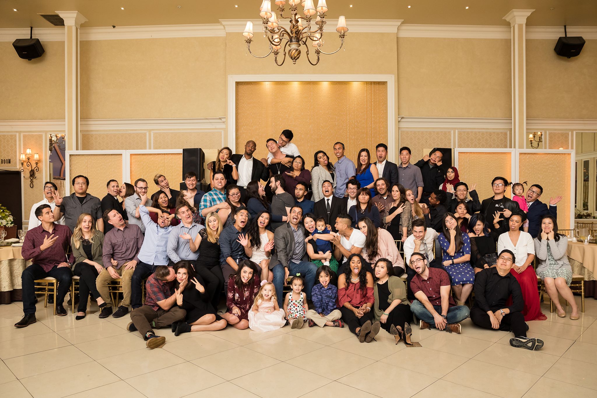 A large group gathered in a ballroom, pulling faces and joking for the camera