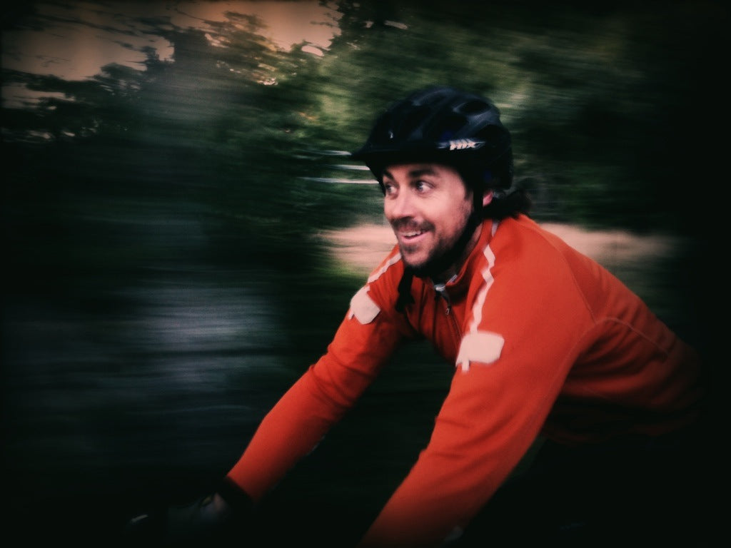 Chris Mann wearing a helmet and red jacket while cycling outdoors
