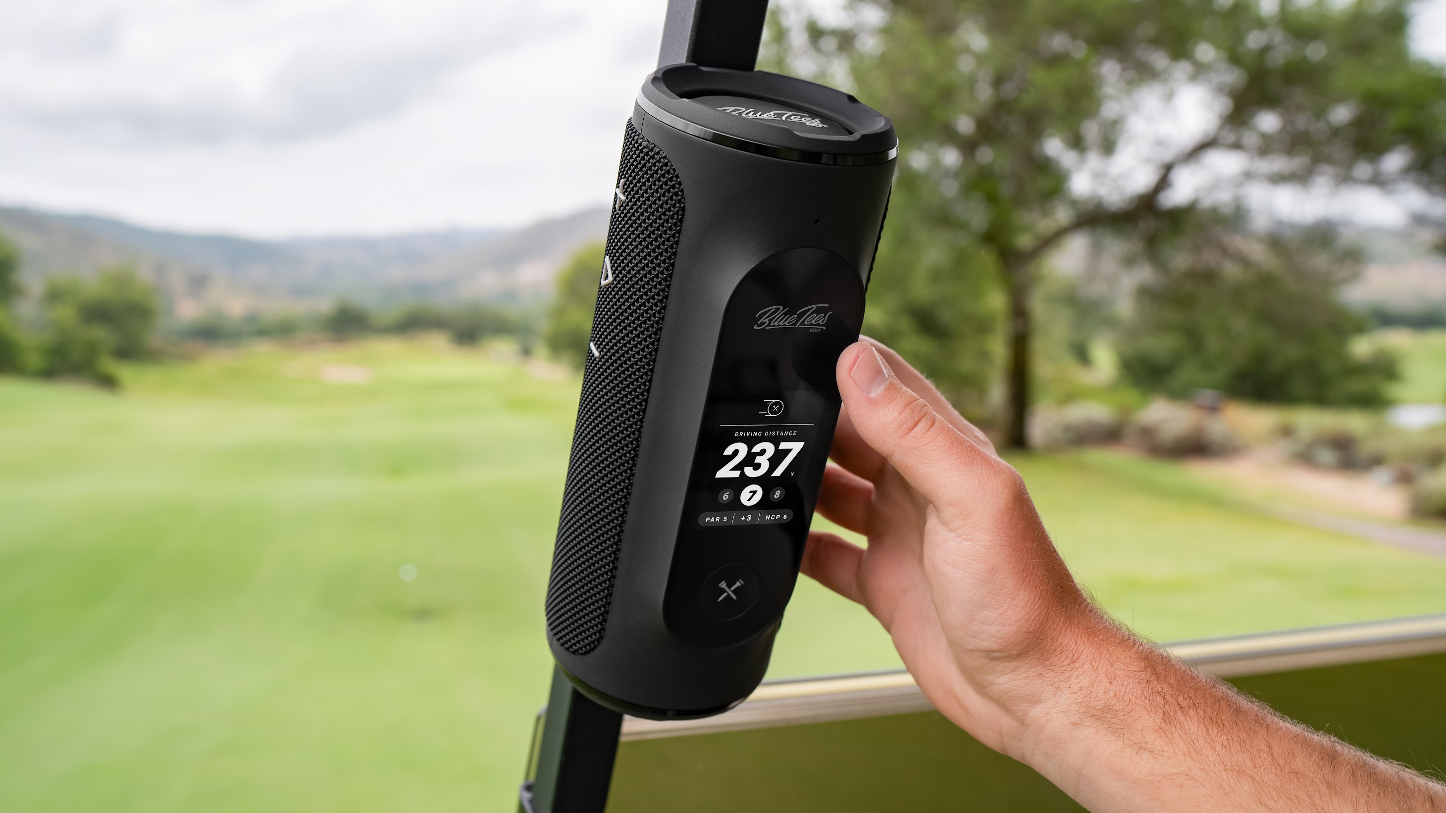 A Blue Tees PLAYER+ GPS speaker mounted to a golf cart, with its touchscreen displaying driving distance