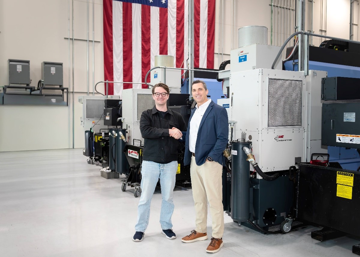 Chris Power and Tom Carrubba shake hands in front of machining equipment and an American flag at Hadrian's Los Angeles headquarters
