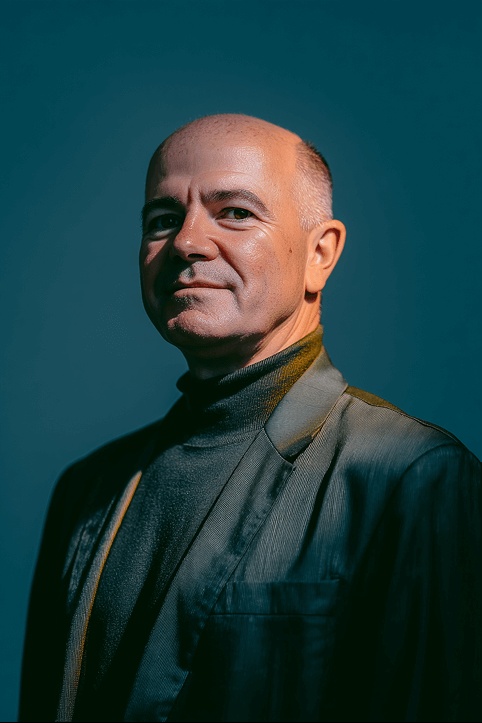 Chris Rasmussen in a dark jacket against a teal background, in a portrait published by Peerscale