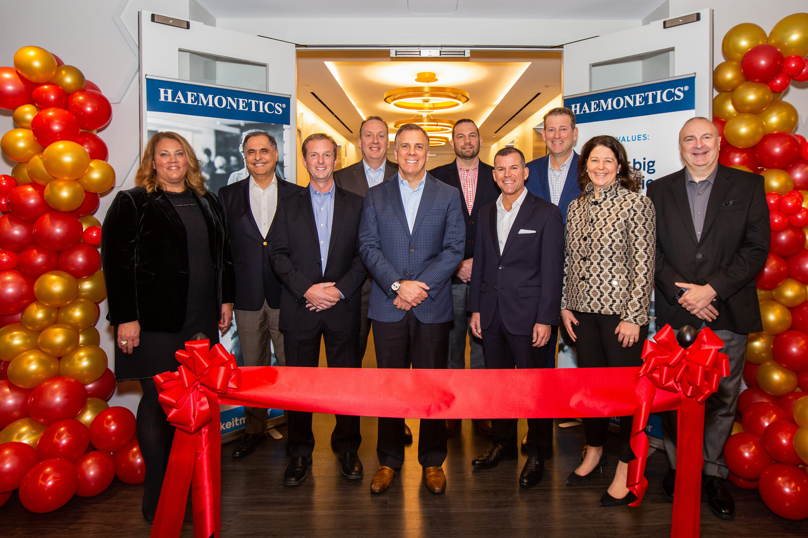 Haemonetics leadership gathered behind a red ribbon at the opening of the Boston headquarters