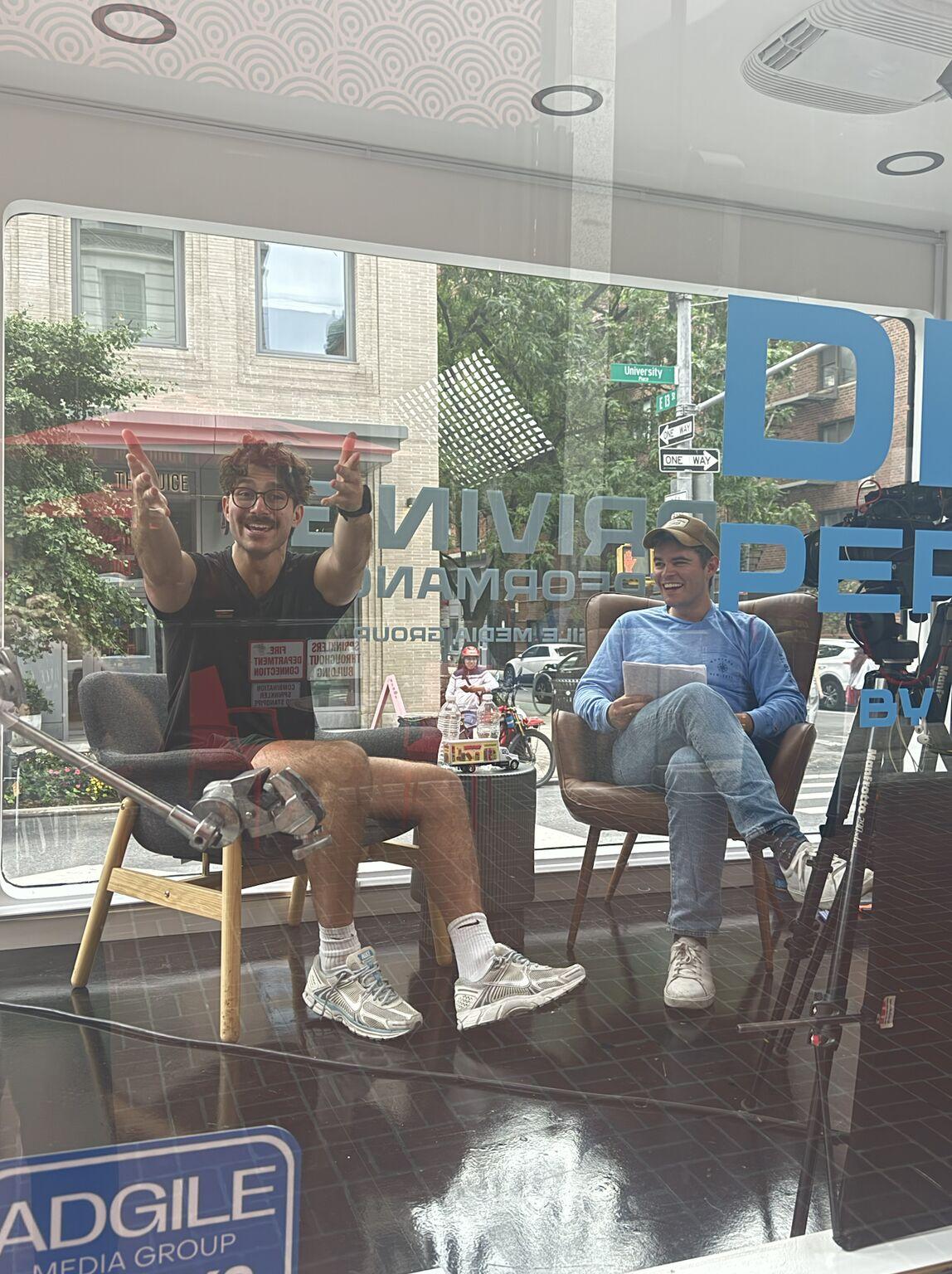 Chris Tiffin gestures beside Tom Shea during the Driving Performance recording inside a glass-sided truck