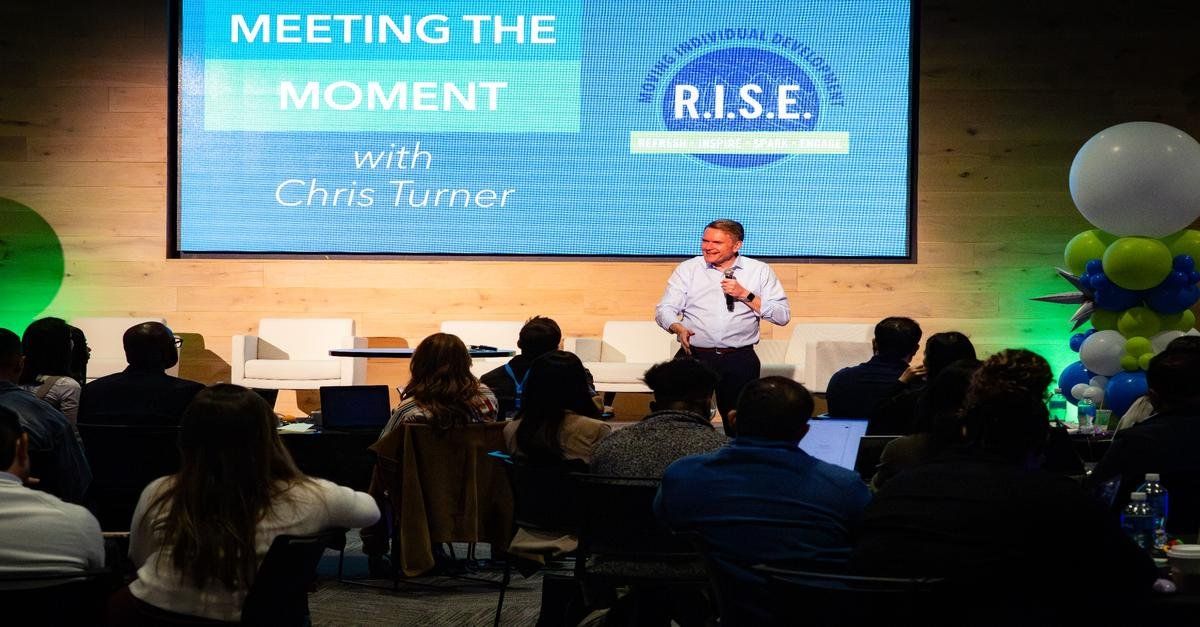 Chris Turner speaking with a microphone to a seated audience at a Meeting the Moment event