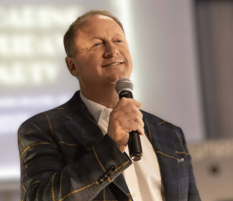 Chris Wahl holding a microphone while wearing a checked jacket
