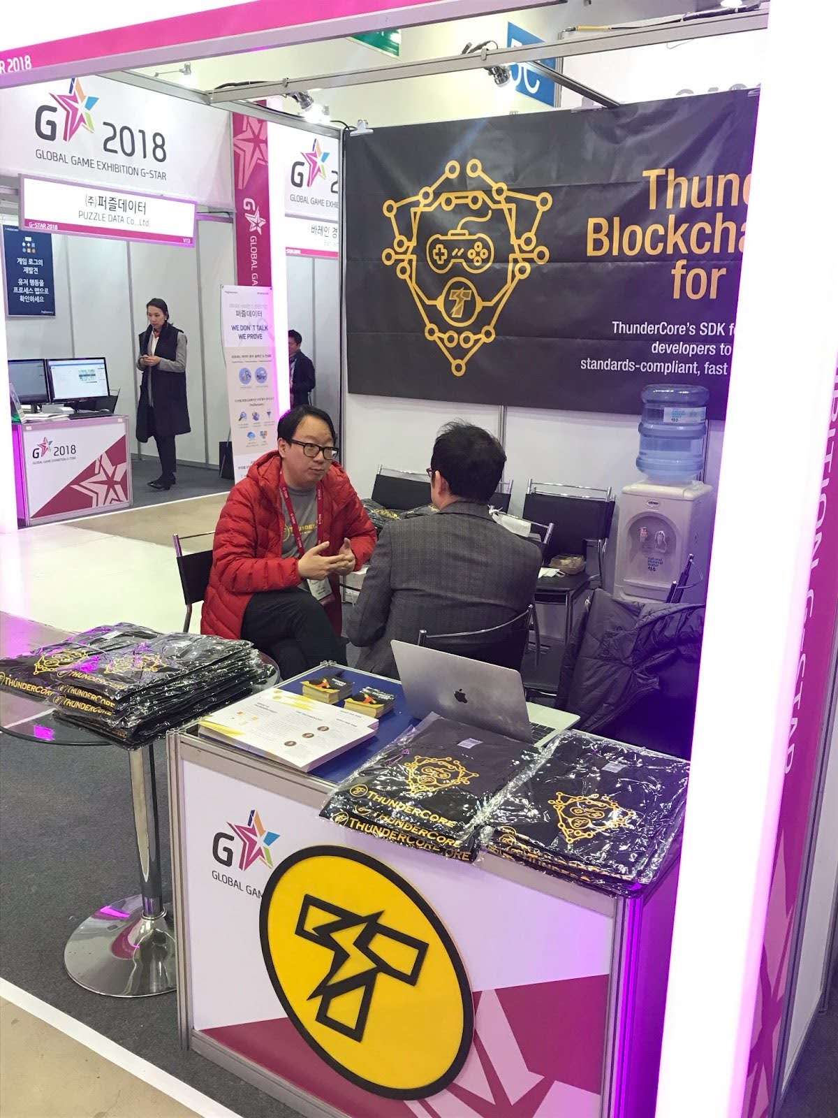 Chris Wang in a red jacket speaking with a visitor at ThunderCore’s booth at G-Star 2018