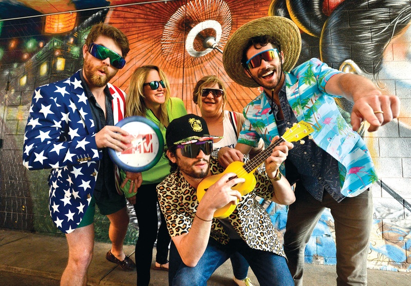 Early Shinesty team in patterned clothing, with Chris White seated at the center holding a yellow ukulele