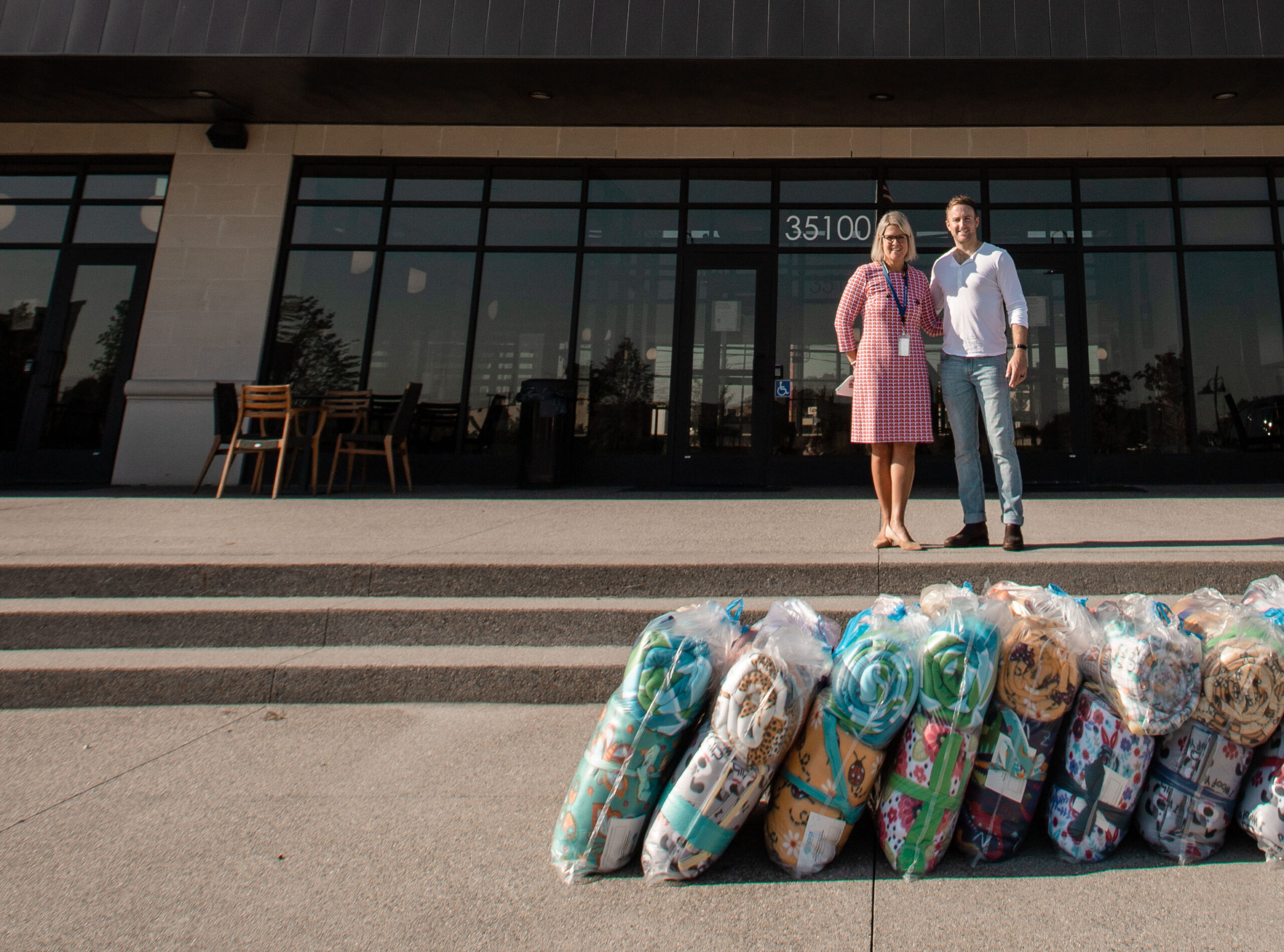 Two people outside Christian Financial headquarters with bags of colorful blankets in the foreground