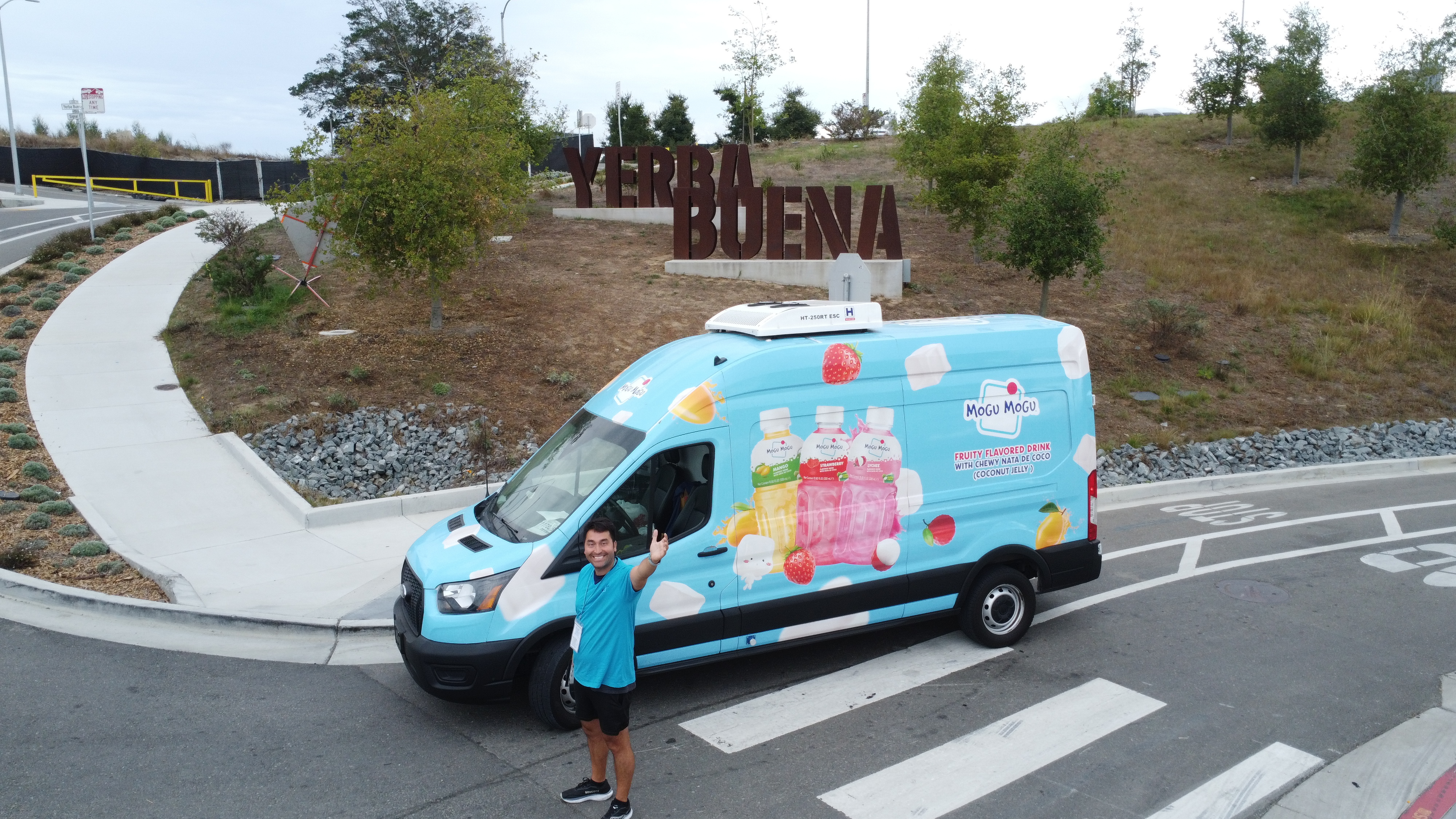 Mogu Mogu's blue sampling van beside the Yerba Buena sign, with a campaign representative in front