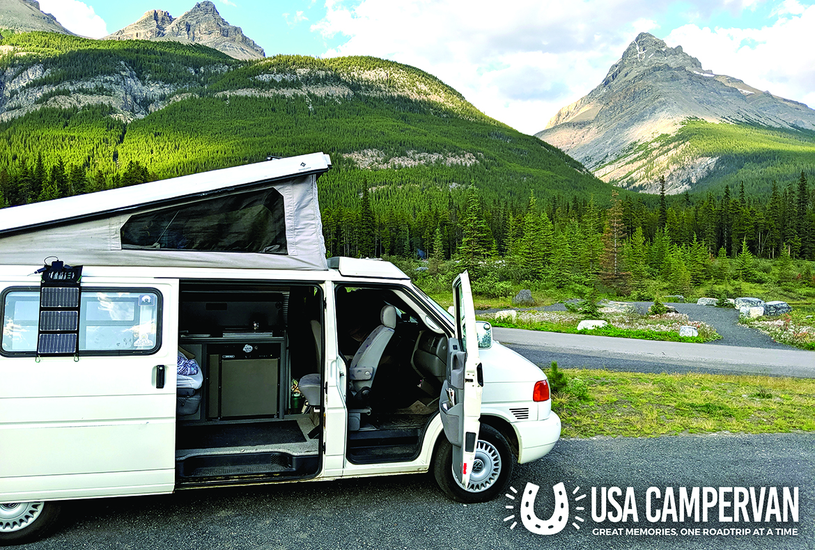A USA CamperVan camper with its roof raised, parked beside a mountain road