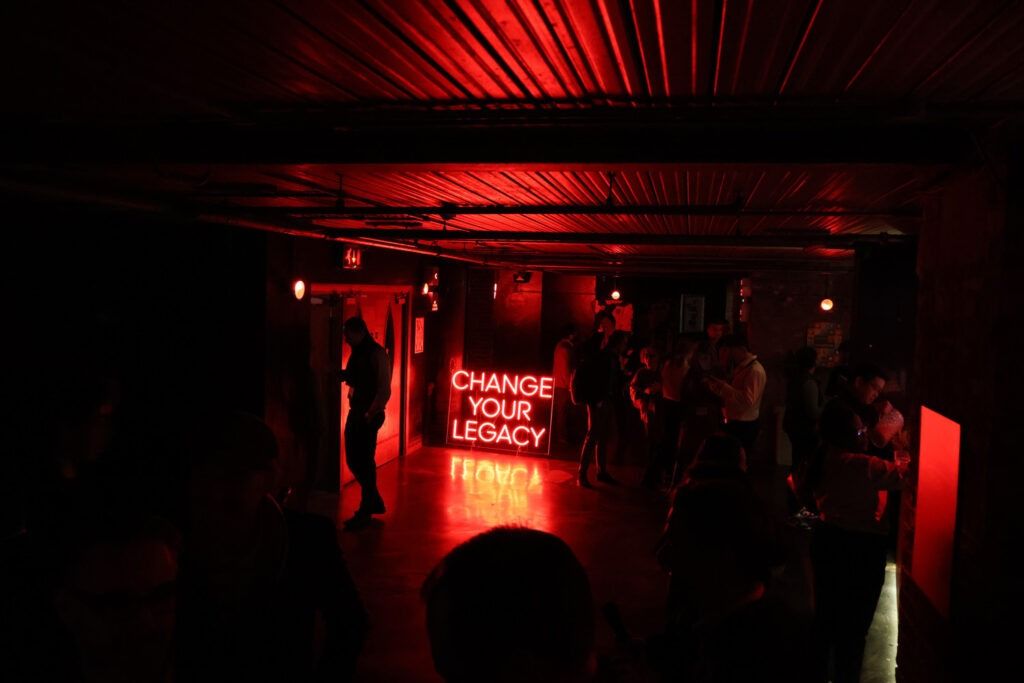 Red-lit gathering space at Duco’s Customer Innovation Day at fabric in London, with a Change Your Legacy neon sign