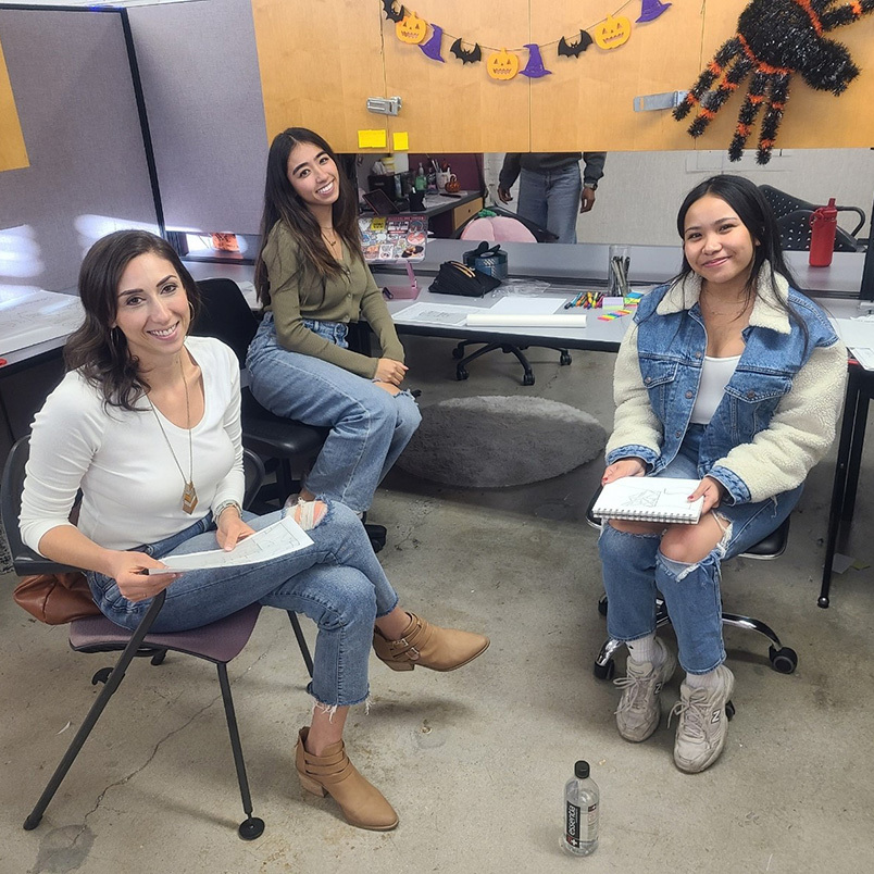 Christie Porter seated with student interns holding notebooks in a studio decorated for Halloween