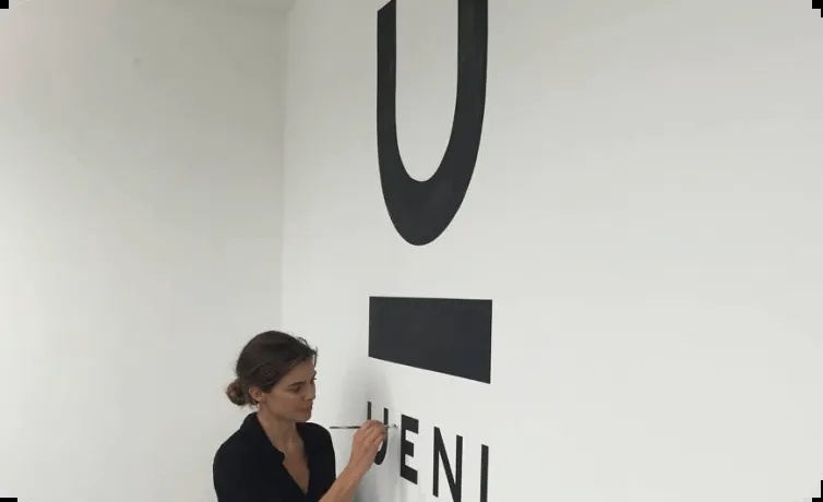 Christine Telyan beside a large early UENI logo on a white wall