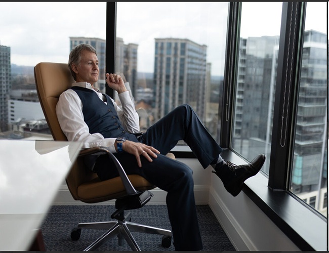 Christopher Graham seated beside office windows, looking across the city