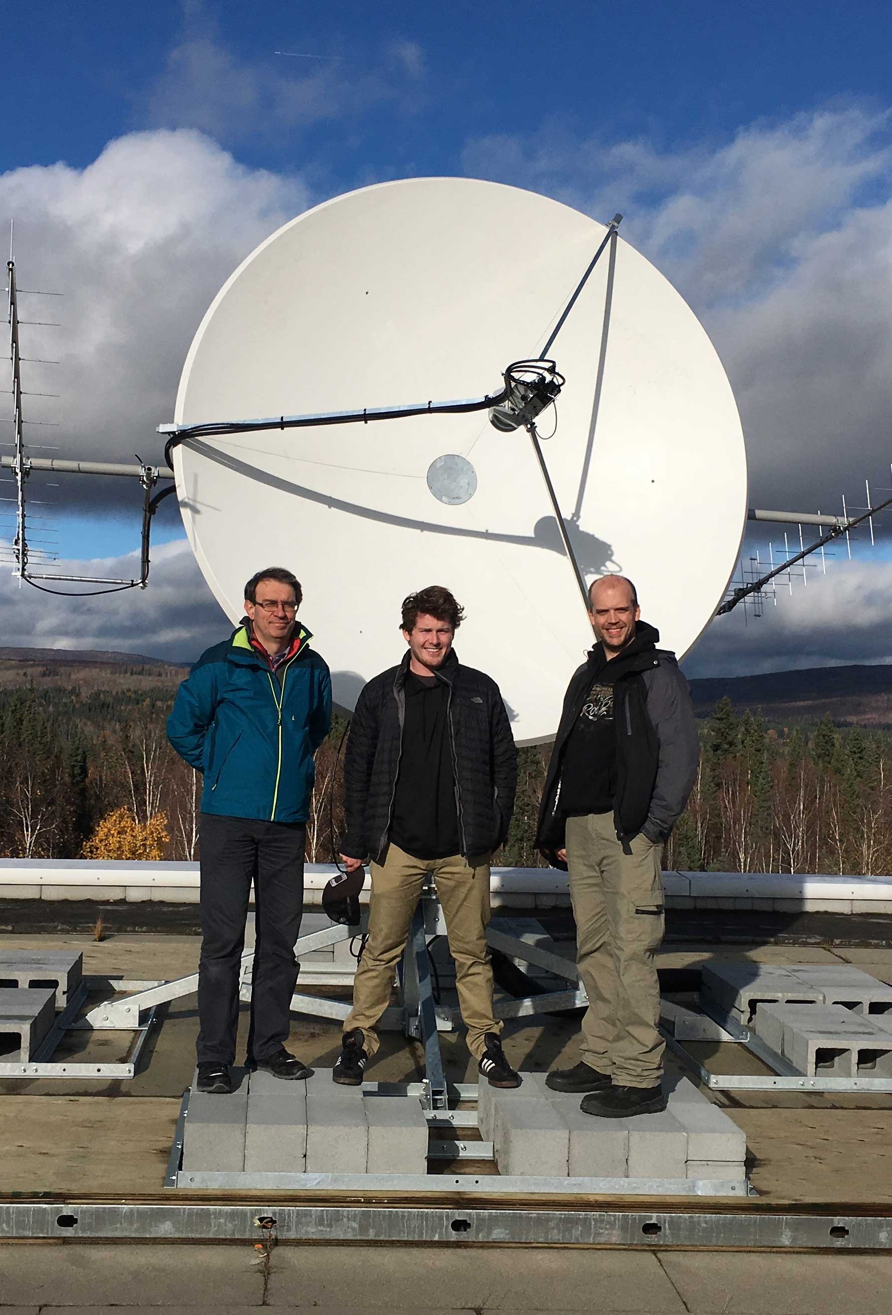 Alex Shumilin, Zach Reich and Christopher Richins standing beside a large satellite ground station antenna