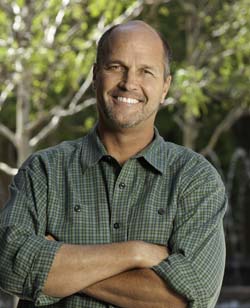 Archival photograph of Chris Stone outdoors, wearing a green shirt with his arms folded.