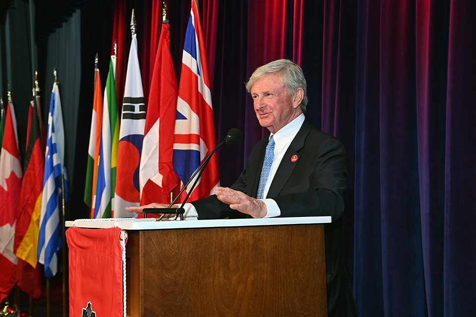 Chuck Davis speaking at a lectern before international flags at St. John’s Insurance Leader of the Year dinner