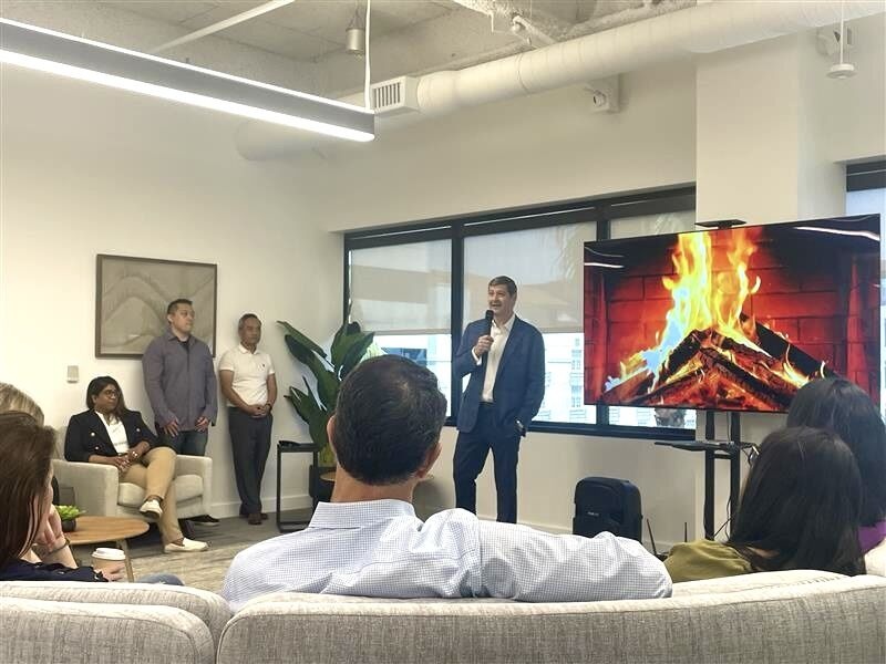 Chuck Divita speaking to colleagues beside a screen displaying a fireplace during his West Coast team visit