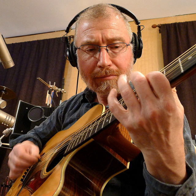 Chuck Donnelly wearing headphones and playing acoustic guitar in a recording studio