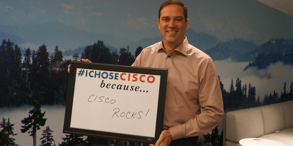 Chuck Robbins smiling while holding an I Chose Cisco sign that reads Cisco Rocks