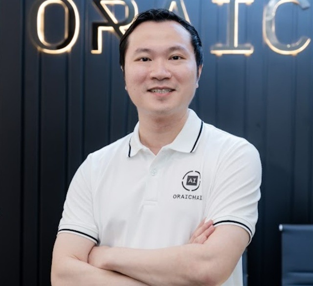 Chung Dao in a white Oraichain polo shirt, standing before the company sign