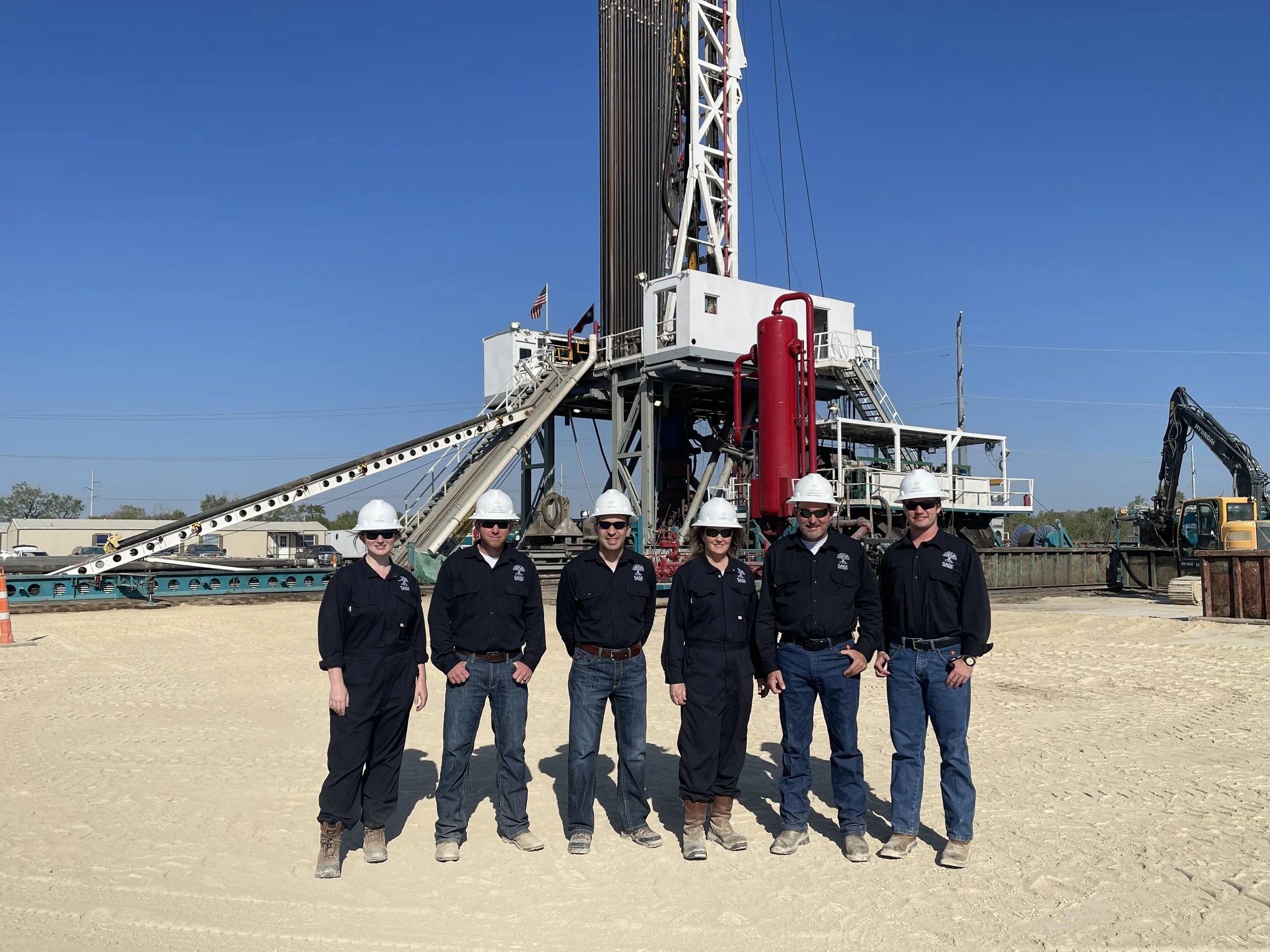 Cindy Taff, fourth from left, standing with five Sage colleagues in front of a drilling rig