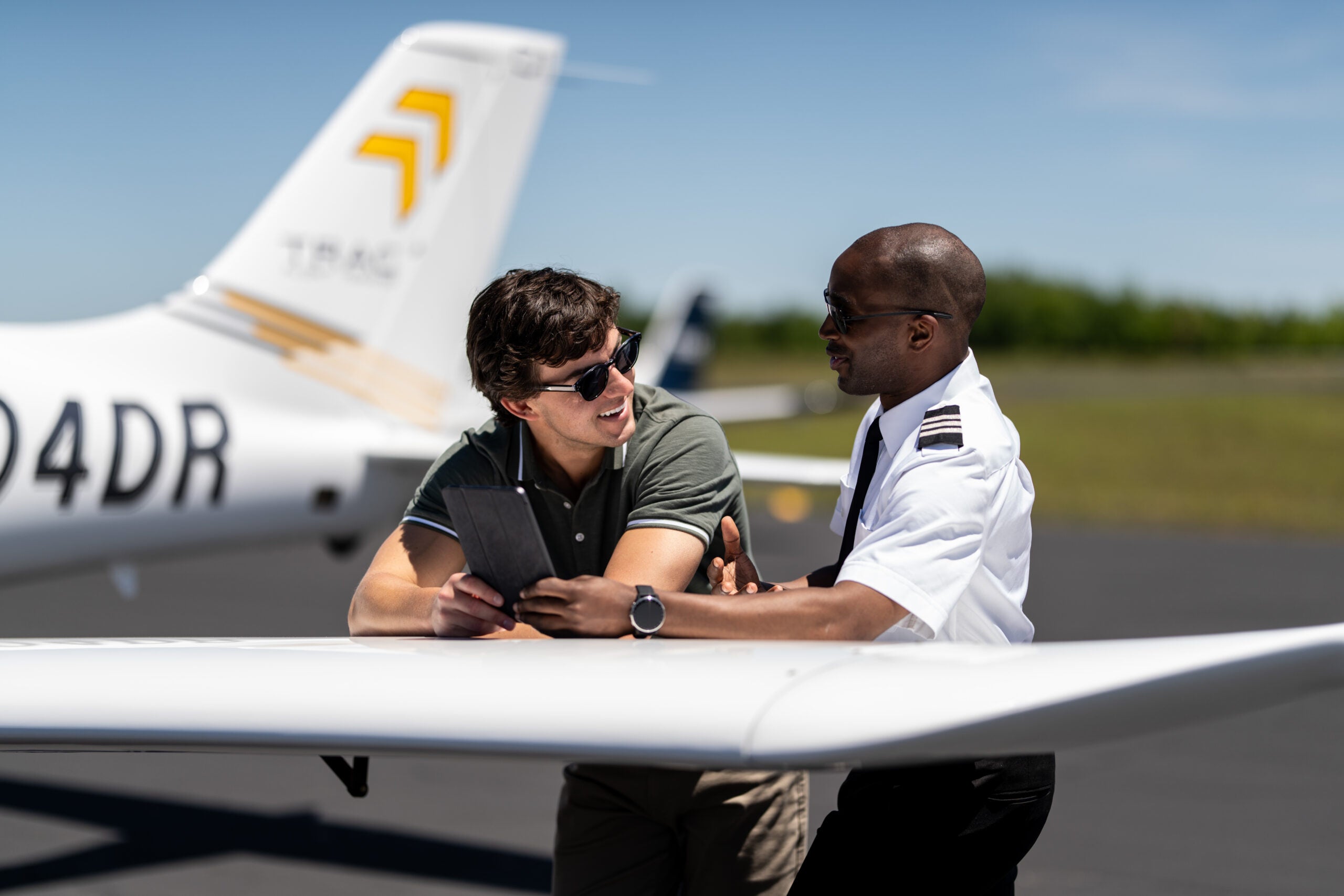 Flight instructor and student reviewing a tablet beside a Cirrus TRAC10 aircraft