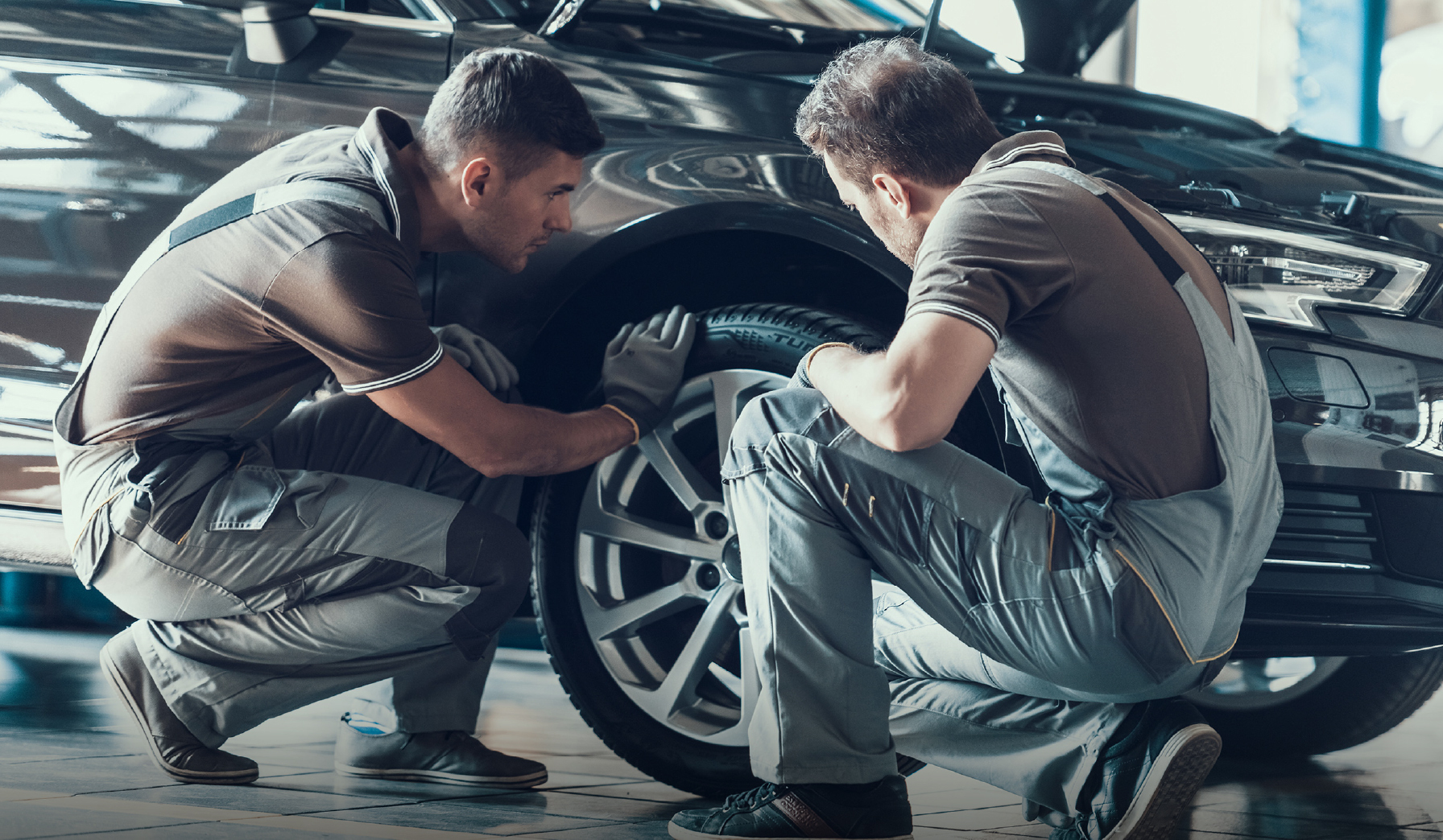 Two technicians examining a car’s front wheel in a workshop.