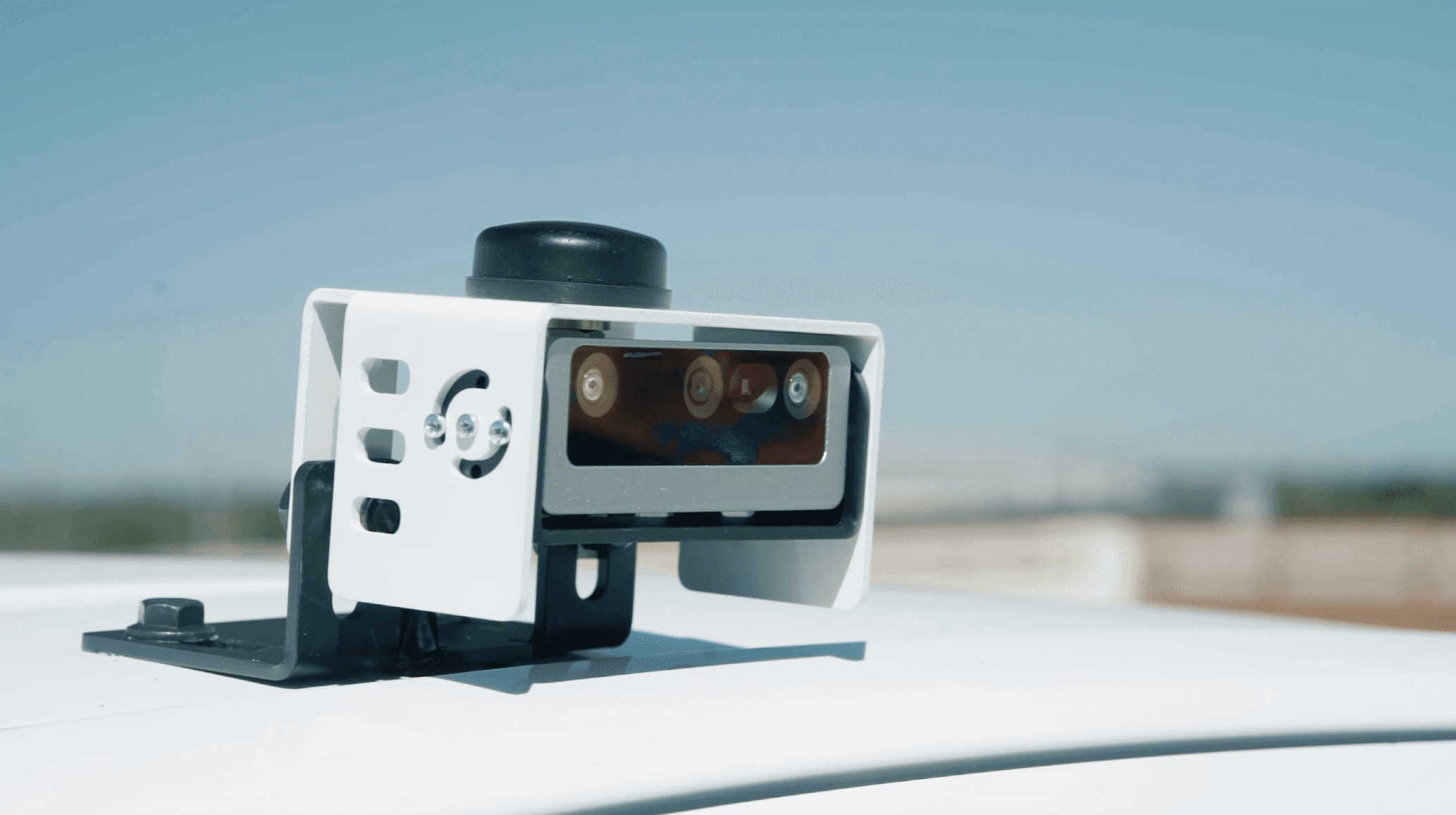 White multi-lens camera unit mounted on a vehicle roof against a blue sky
