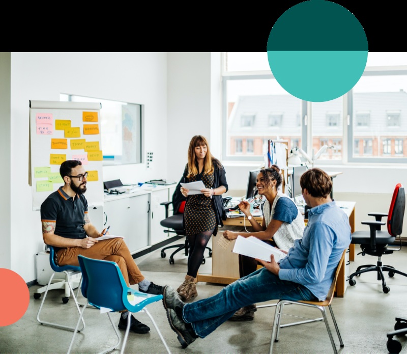Four colleagues in a bright office meeting space, with notes on a flip chart