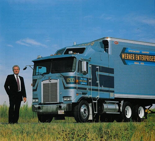 CL Werner in a suit standing beside a blue Werner Enterprises truck and trailer
