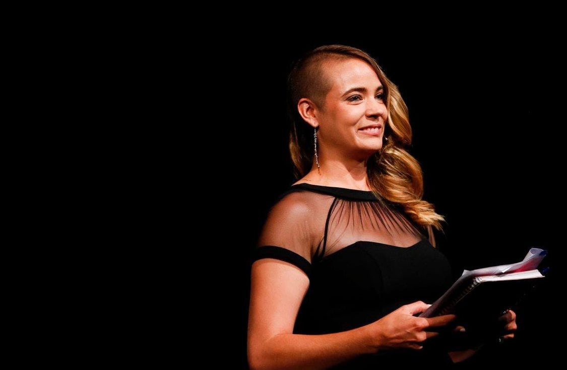Clair Byrd speaking on a dark stage, holding notes