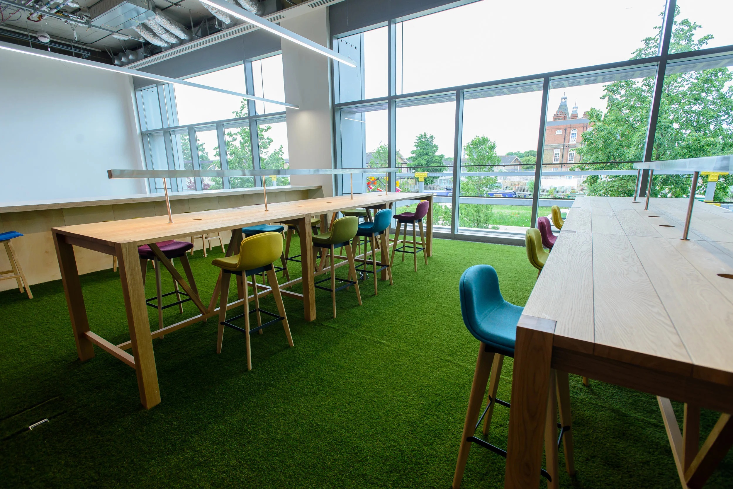 Shared tables and colourful chairs beside tall windows at Plexal in 2017