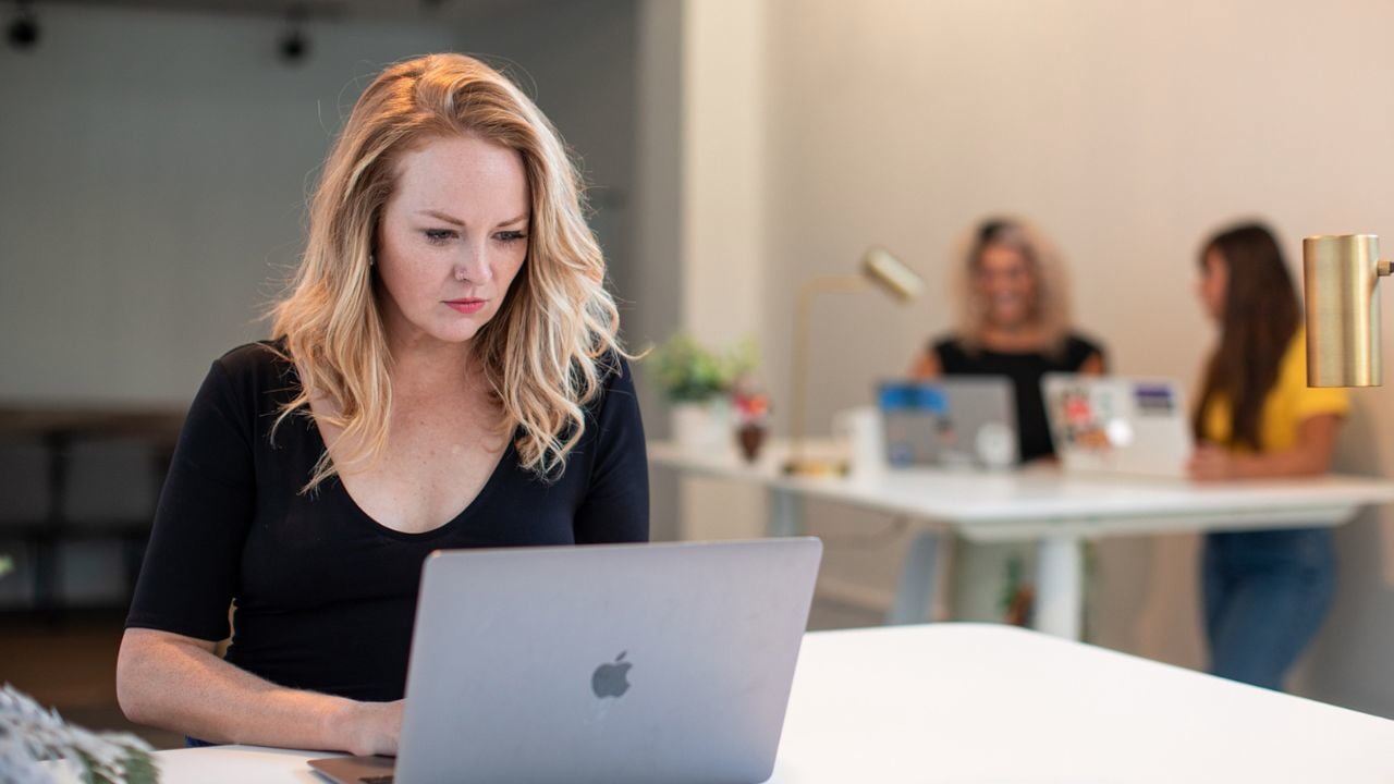 Claire Winslow Brown working at a laptop, with two people at a table behind her